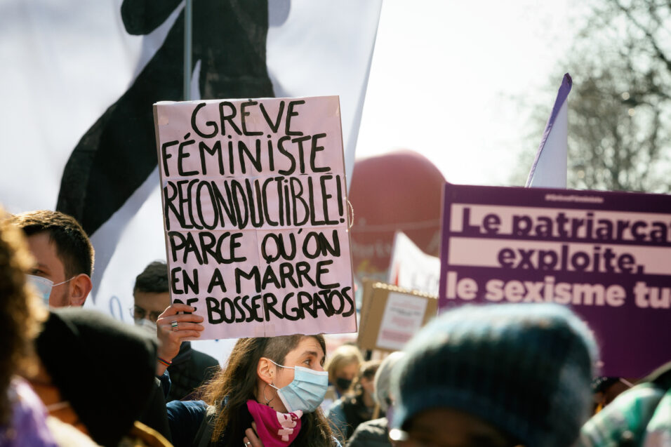 Une personne tenant une pancarte "Grève féministe reconductible parce qu'on en a marre de bosser gratos"